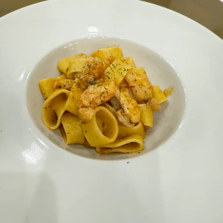 Calamarata con rana pescatrice servita in piatto bianco, condita con pomodorini e polvere di prezzemolo